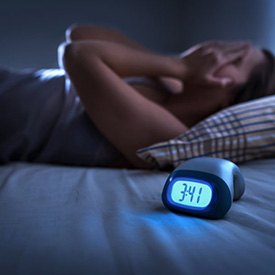 Woman struggling to sleep as clock displays 3:00 am